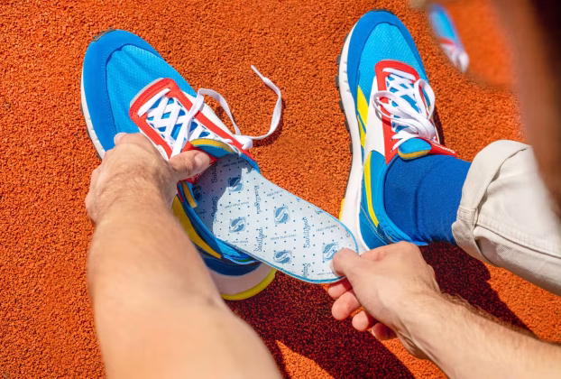 Dłonie wkładające wkładki do butów Coccine w sportowe obuwie.
